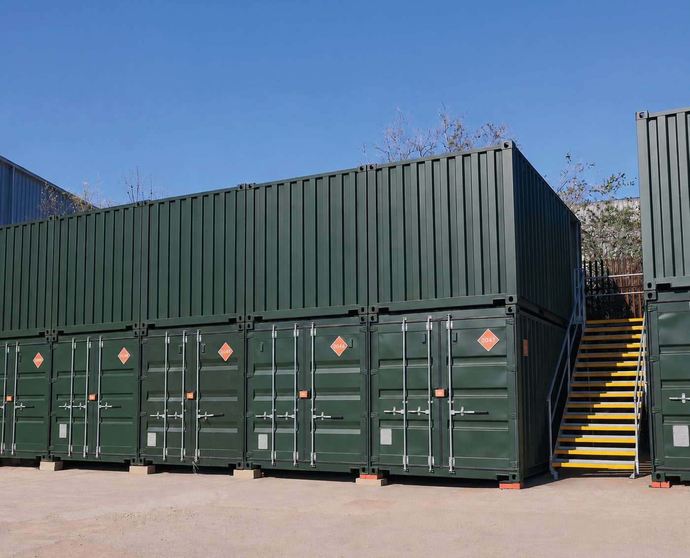 Two-high rows of green self-storage containers with a yellow stair, under a clear blue sky